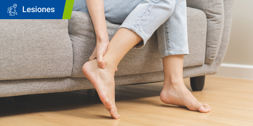 Mujer tocándose el tobillo porque tiene dolor en las articulaciones. Se lee el texto “Lesiones” en un recuadro.  Mujer tocándose el tobillo porque tiene dolor en las articulaciones. Se lee el texto “Lesiones” en un recuadro.